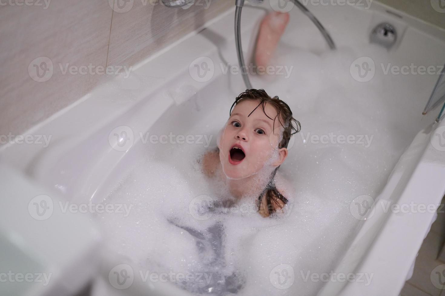 kleines Mädchen im Bad, das mit Seifenschaum spielt foto
