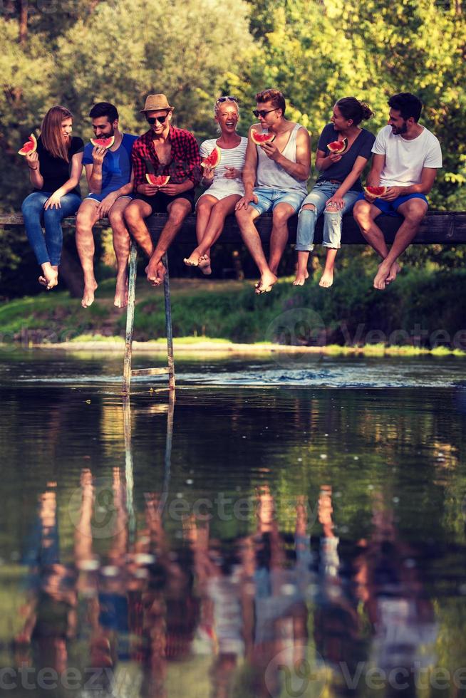 freunde, die wassermelone genießen, während sie auf der holzbrücke sitzen foto