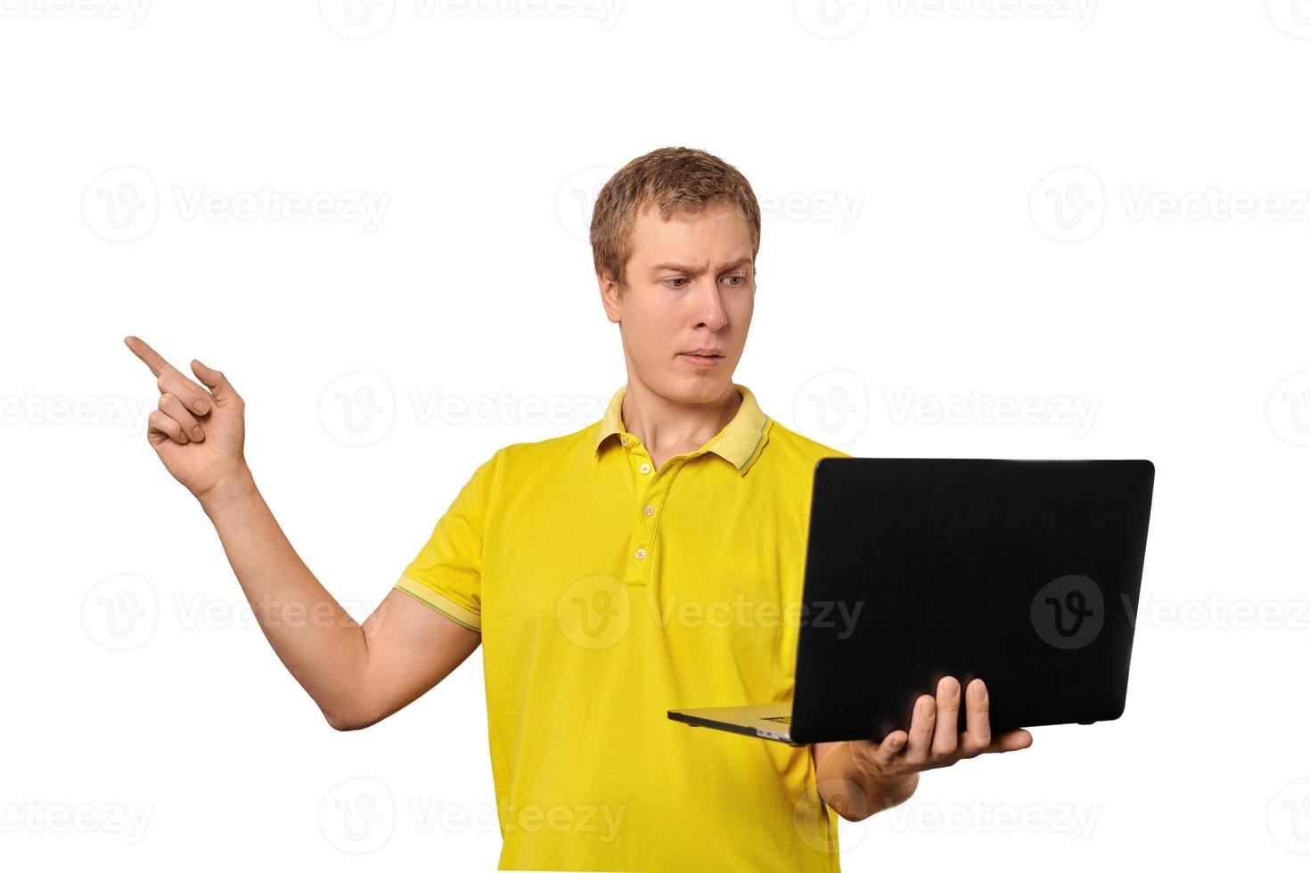 Verwirrter junger Mann mit Laptop, der mit dem Finger isoliert auf weißem Hintergrund zeigt, männliches verwirrtes Gesicht foto