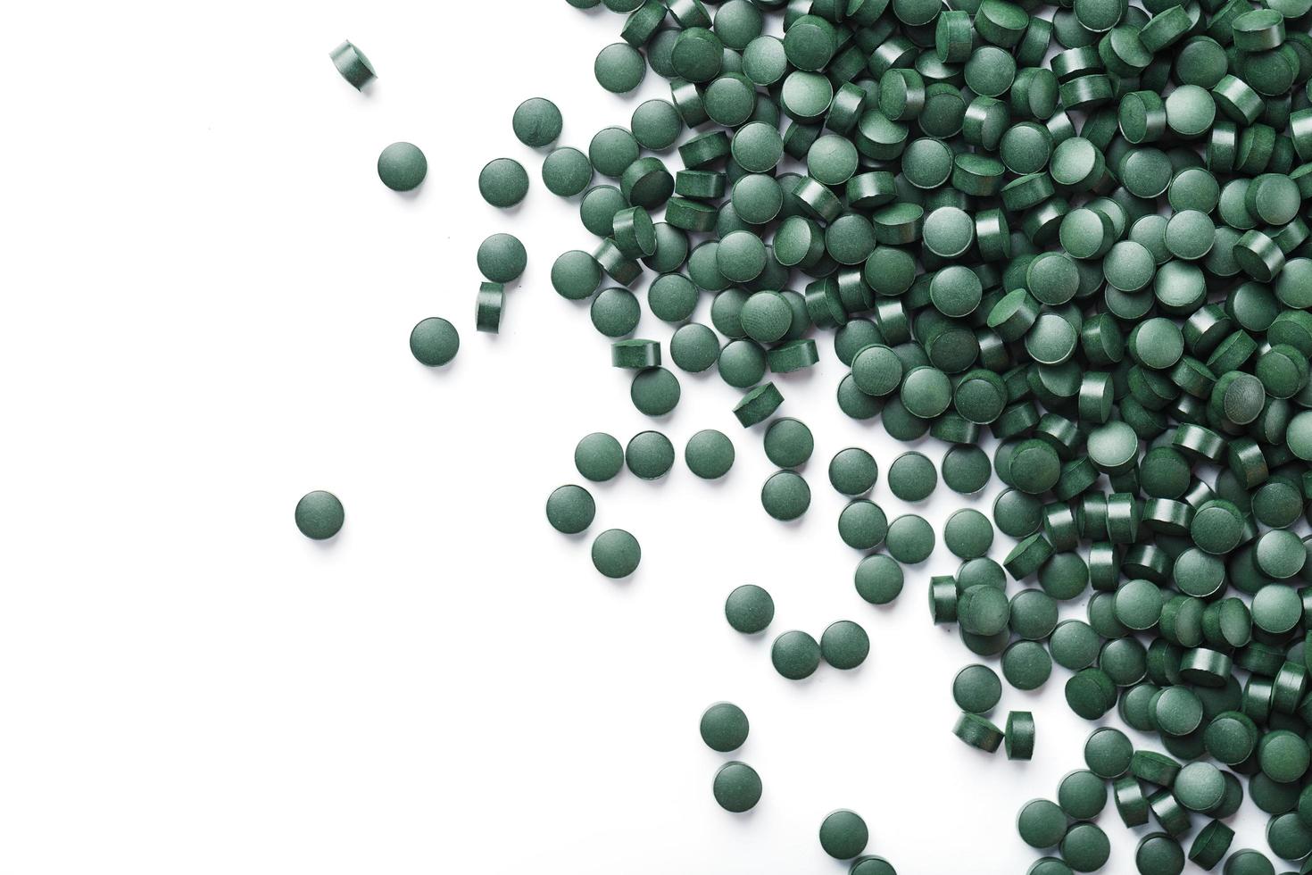 Vegetarische Vitamine aus Spirulina sind auf weißem Hintergrund verstreut foto