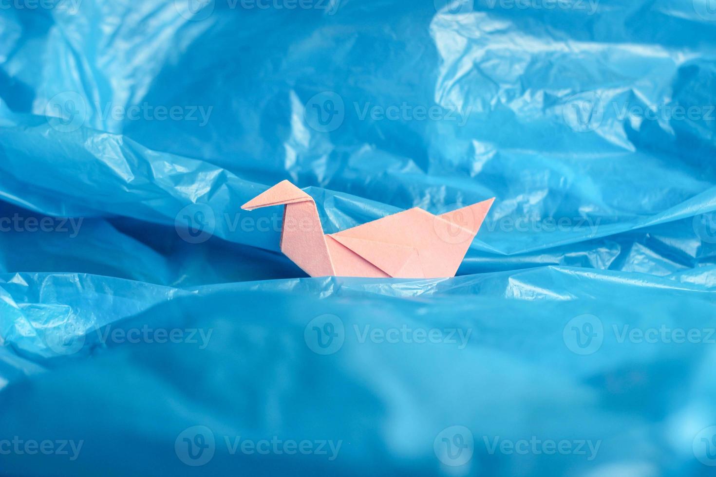 Vogelorigami aus rosafarbenem Papier zwischen einer blauen Plastiktüte wie auf Wellen aus Wasser oder blauem Himmel. Konzeptfoto foto