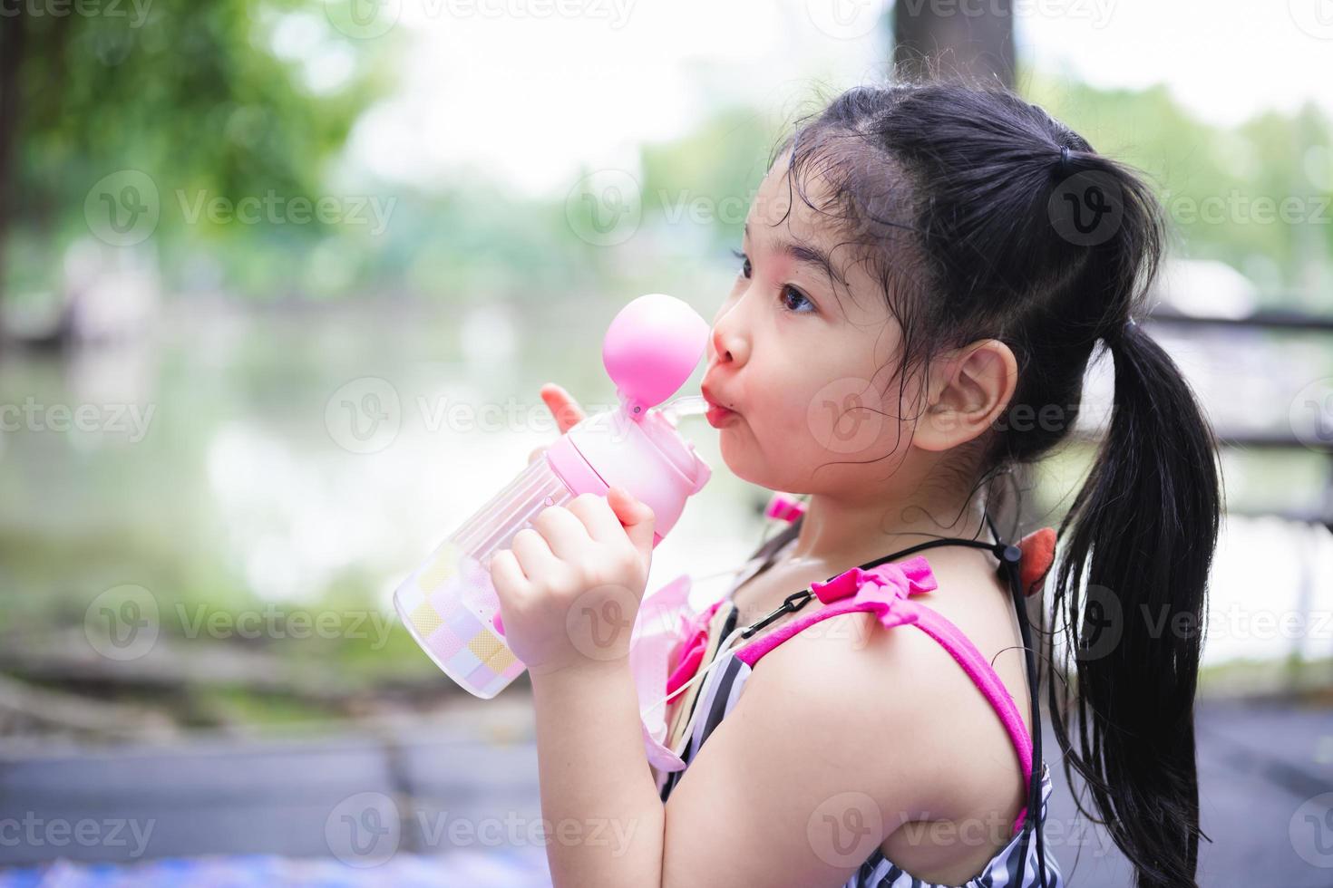 Porträtbild asiatisches Kind 5 Jahre alt. Trinkwasser des kleinen Kindes mit Plastikflasche. Kinder saugen Wasser mit Schlauch. Sommersaison. Mädchen sind an heißen Tagen durstig. leerer raum für die eingabe von text. foto
