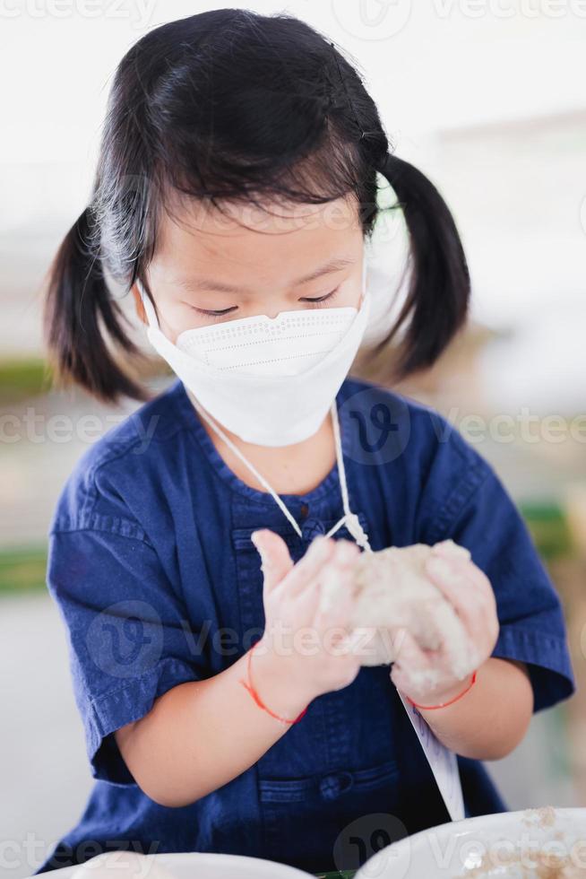 Porträtbild Kind 5 Jahre alt. asiatische Mädchen lernen, wie man Lebensmittel konserviert oder gesalzene Eier herstellt, indem man weißen Gips auf die Eierschale putzt. Kinder tragen eine Maske, um die Luftverschmutzung durch giftigen Staub pm2.5 zu verhindern. foto