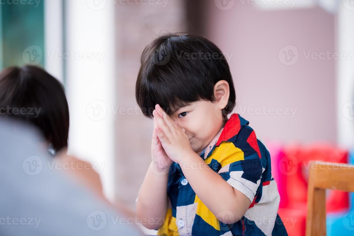 asiatischer Junge hebt die Hände, um Hallo zu sagen, Respekt zu zollen oder Ihnen zu danken. Kind lächelt süß. entzückender sohn im alter von 2-3 jahren, der bunte kleidung trägt. foto
