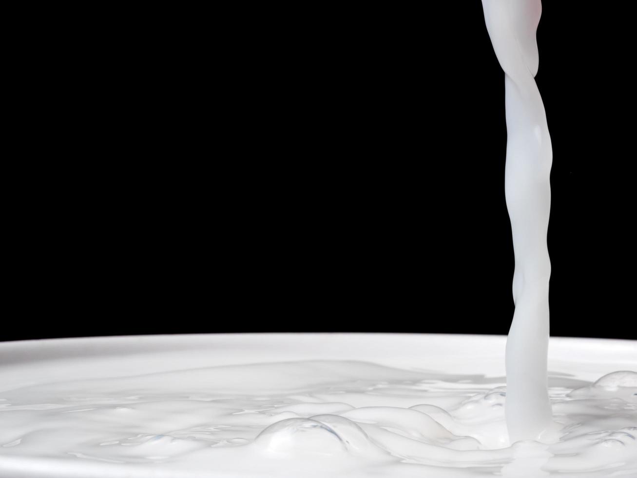 Spritzer Milch aus einer Tasse auf schwarzem Hintergrund. foto