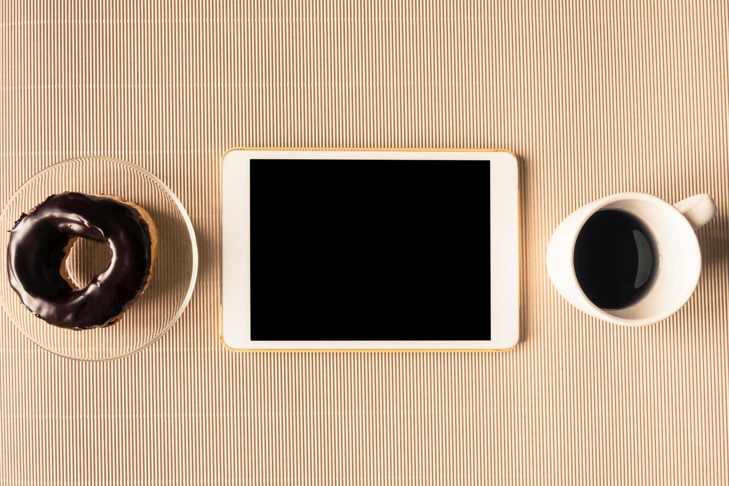 Draufsicht des Tablets mit Kaffeetasse und Donut auf dem Tisch. foto
