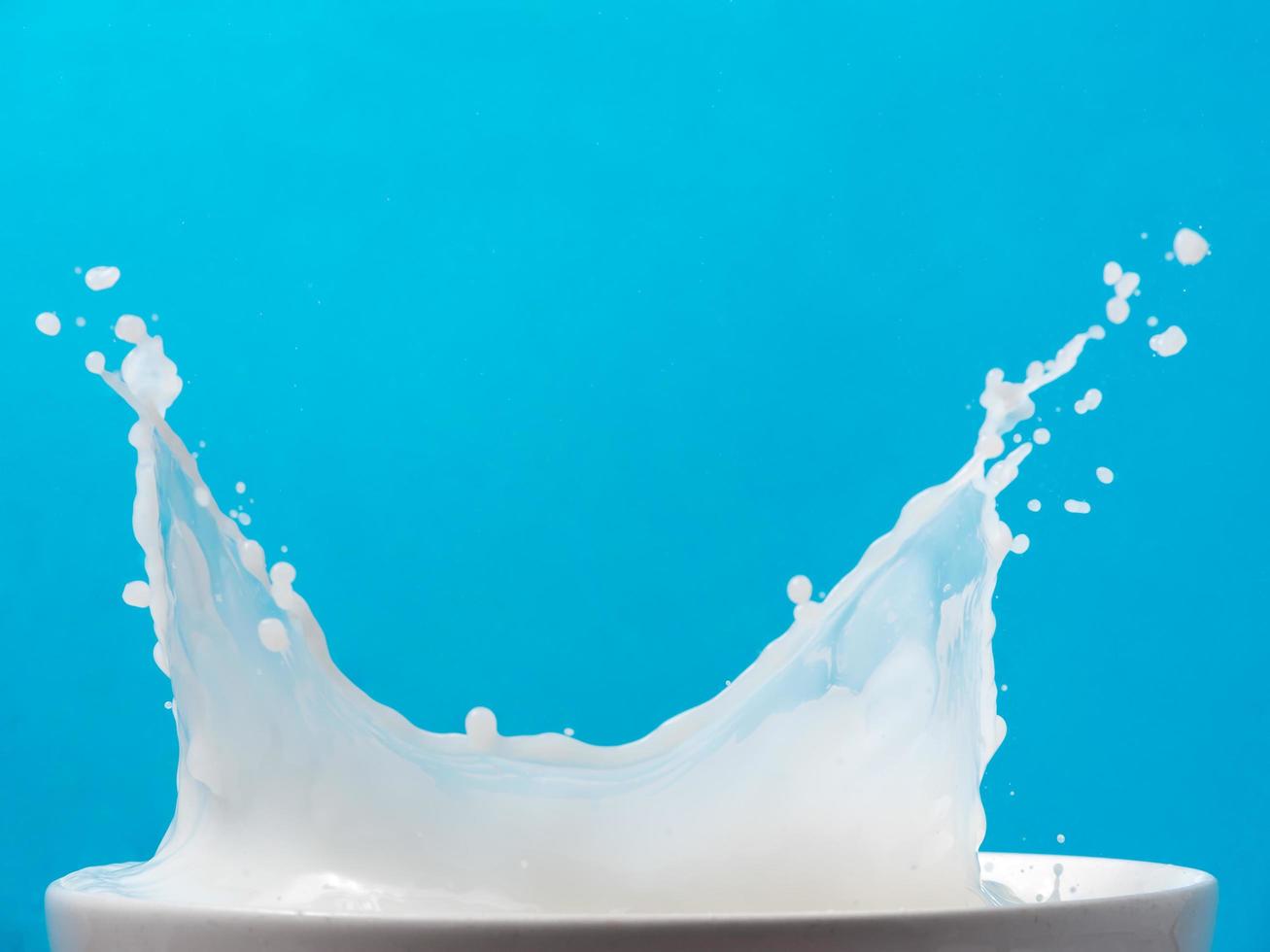 Spritzer Milch aus einer Tasse auf blauem Hintergrund. foto