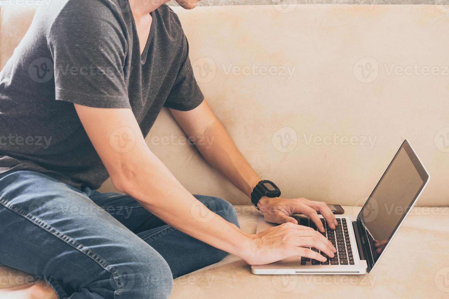 Nahaufnahme eines legeren jungen Mannes, der auf dem Sofa sitzt und zu Hause einen Laptop benutzt. foto