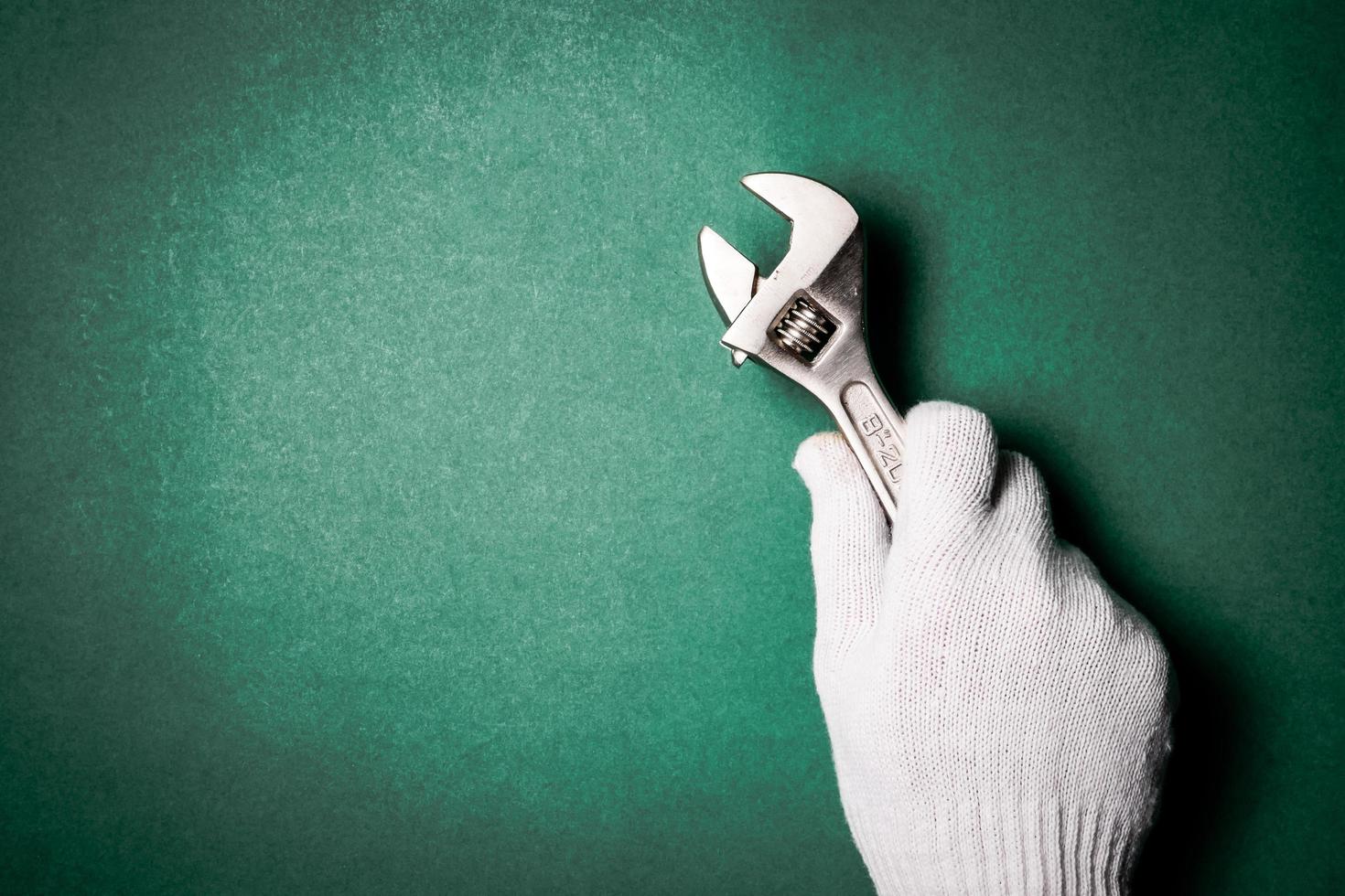 Schraubenschlüssel in der Hand mit Schutzhandschuh auf grünem Hintergrund. Freiraum für Text foto