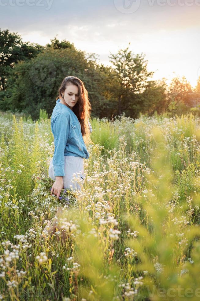 schönes Mädchen, das im Sommer mit Wildblumen auf dem Feld spazieren geht. foto