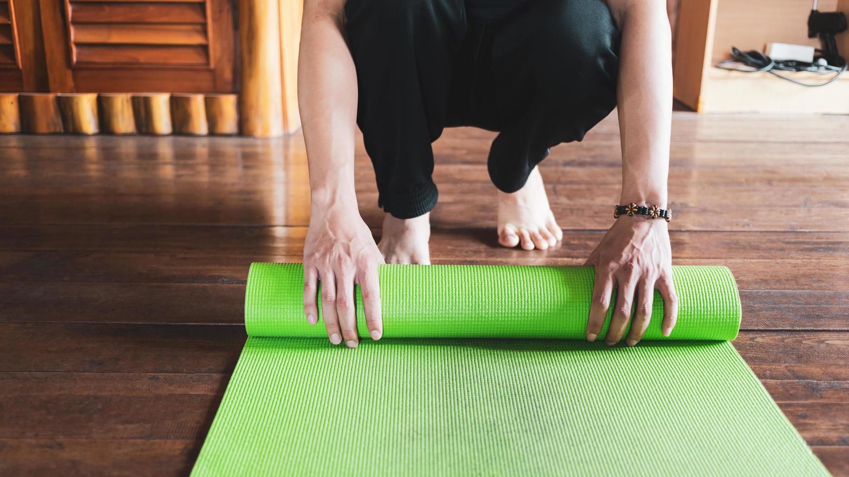 Nahaufnahme eines Mannes, der eine grüne Yogamatte oder Trainingsmatte von Hand rollt, nachdem er morgens Wellness-Yoga-Praxis zu Hause trainiert hat. gesundes leben und gesundes wohnkonzept. foto