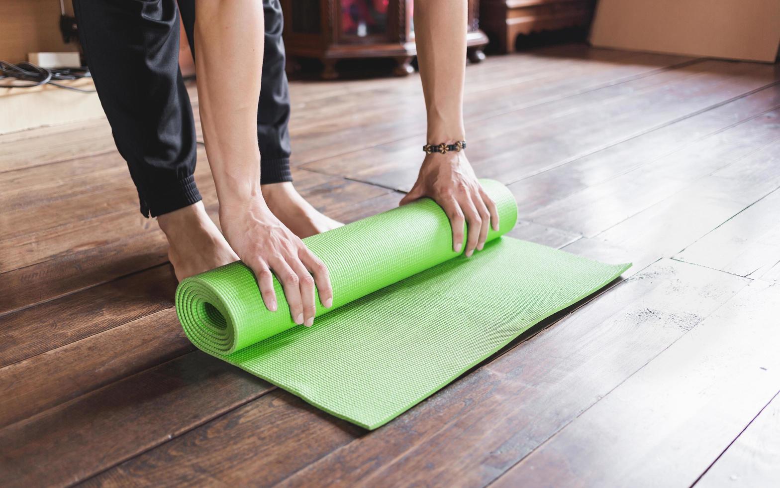 Nahaufnahme eines Mannes, der eine grüne Yogamatte oder Trainingsmatte von Hand rollt, nachdem er morgens Wellness-Yoga-Praxis zu Hause trainiert hat. gesundes leben und gesundes wohnkonzept. foto