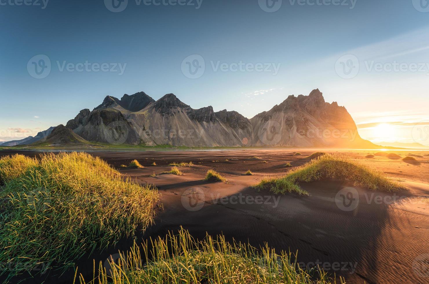 Sonnenaufgang über dem Berg Vestrahorn und Grasbüschel am schwarzen Sandstrand in Stokksnes im Südosten Islands foto