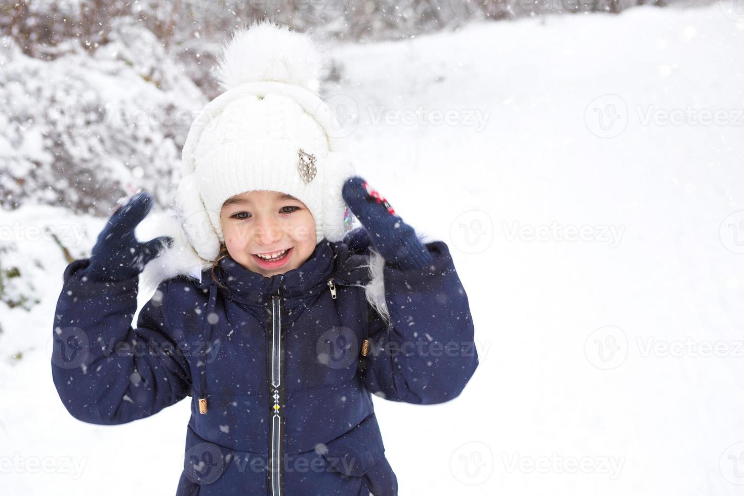 kleines Mädchen im kalten Winter in warmer Kleidung, mit pelzgefütterten Ohrpolstern. Freude, Lachen, Kindergefühle, Winterspiele im Schnee. frostbeständige wasserdichte Membranbekleidung. Platz kopieren foto