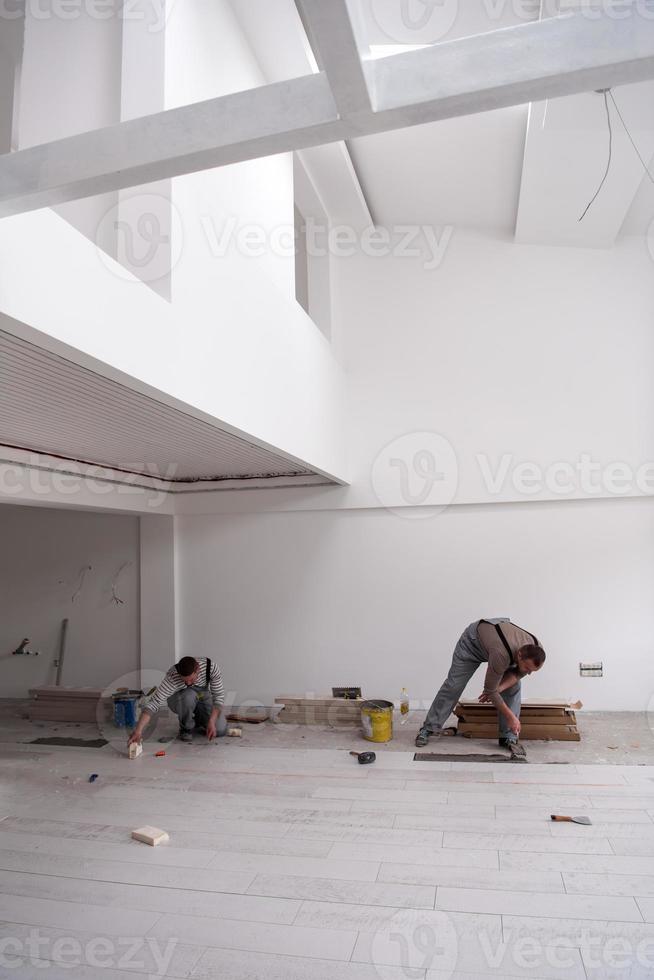 Arbeiter, der die Keramikfliesen in Holzoptik auf dem Boden installiert foto