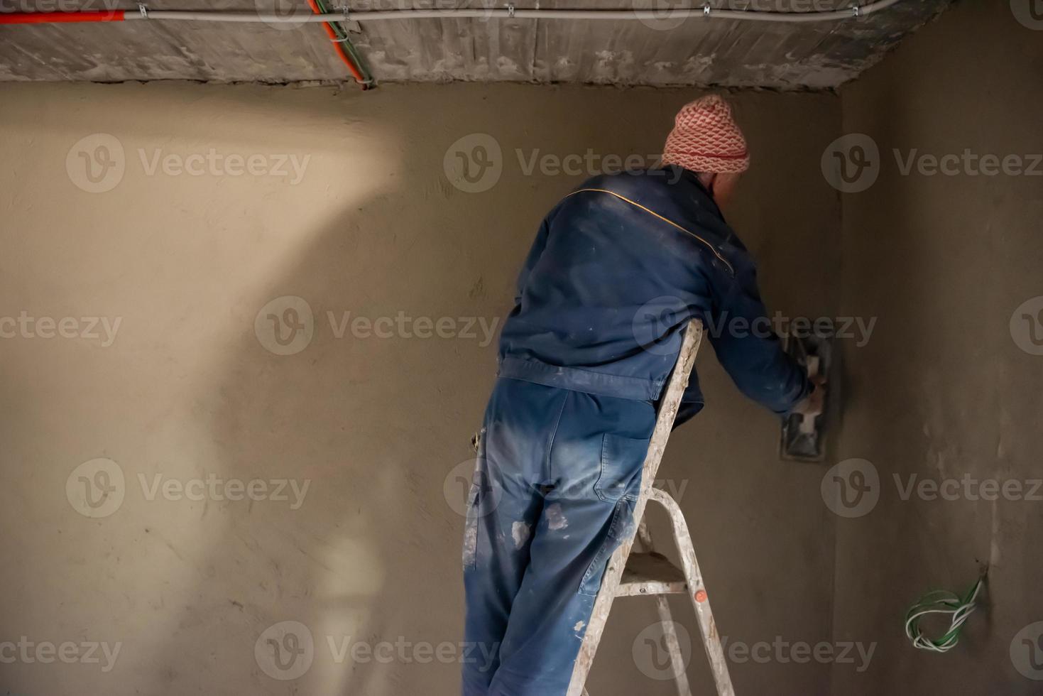 arbeiter, der die wand mit beton verputzt foto