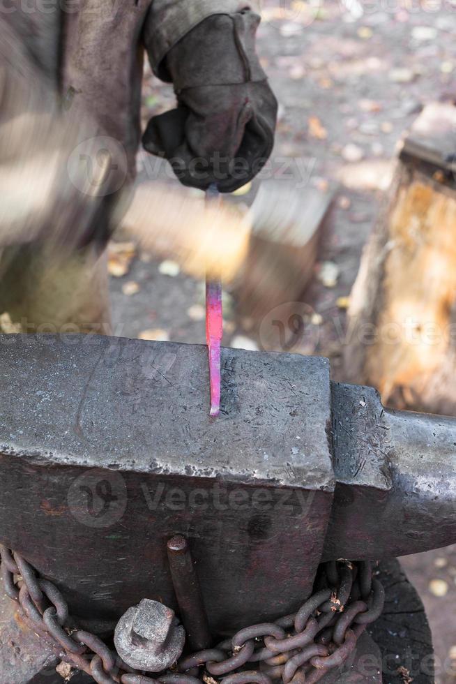 Schmied schmiedet Stahlstange, um Nagel auf Amboss herzustellen foto