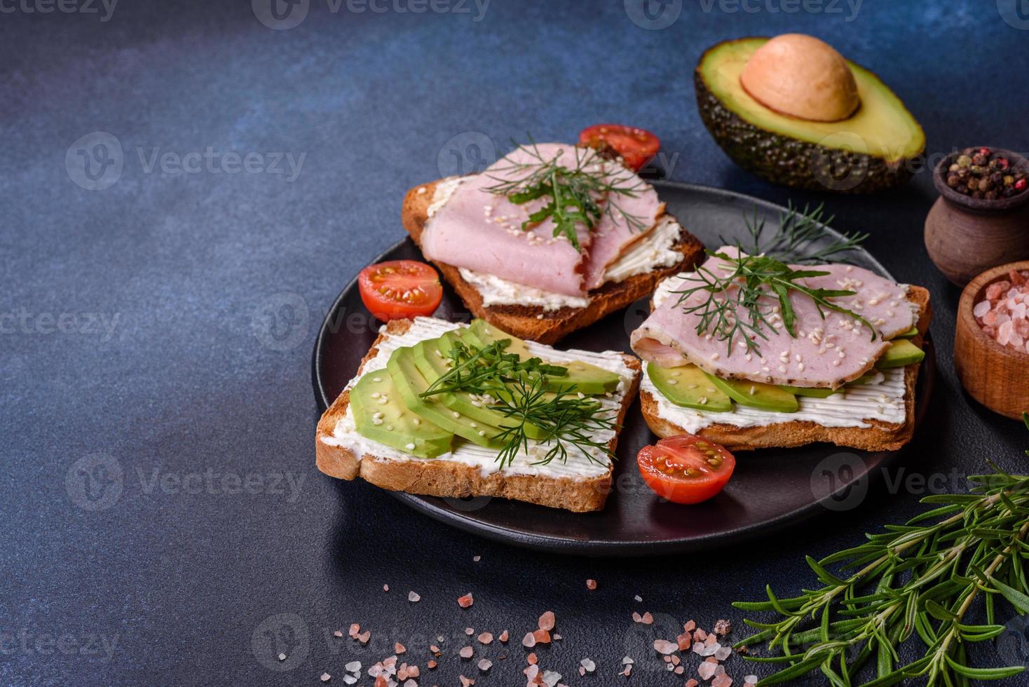 Frische, leckere Sandwiches mit Schinken, Butter, Avocado und Sesamsamen auf einem Holzschneidebrett foto