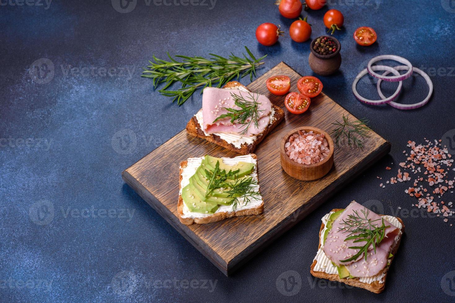 Frische, leckere Sandwiches mit Schinken, Butter, Avocado und Sesamsamen auf einem Holzschneidebrett foto