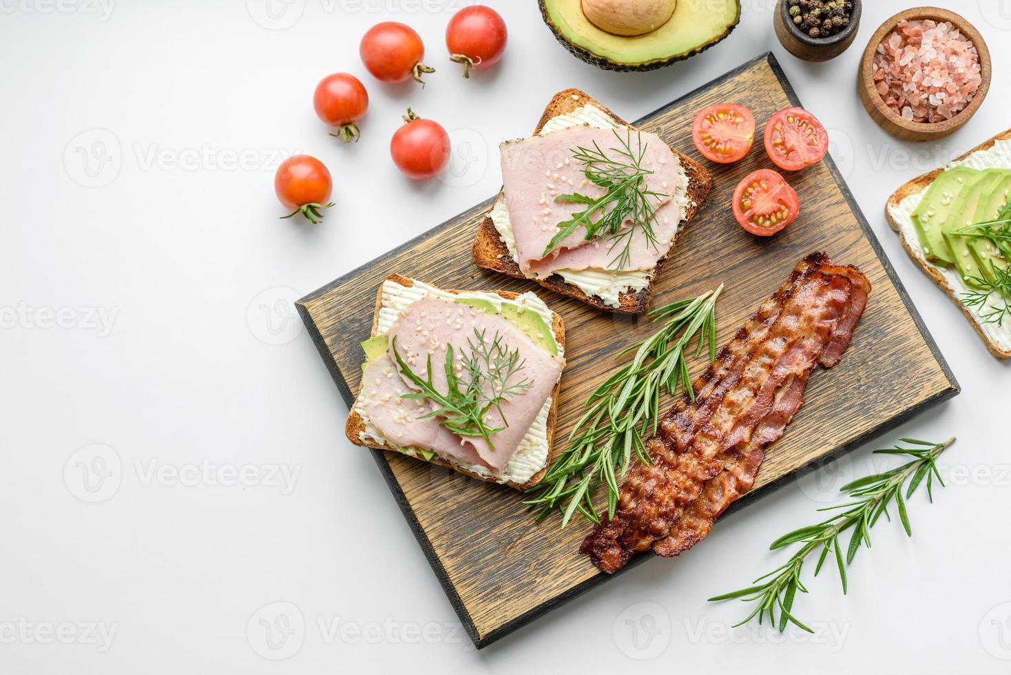 Frische, leckere Sandwiches mit Schinken, Butter, Avocado und Sesamsamen auf einem Holzschneidebrett foto