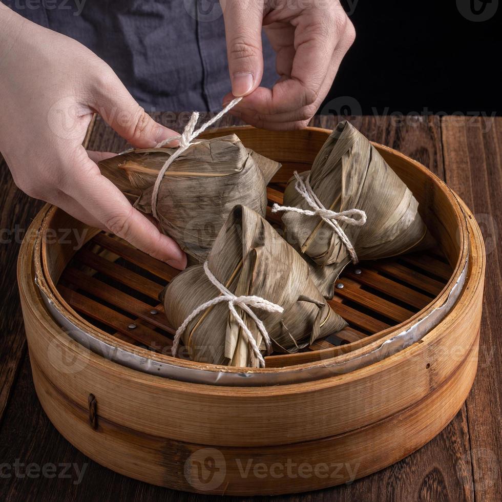 Reisknödel, Zongzi - Drachenbootfest, Haufen chinesischer traditioneller gekochter Speisen im Dampfgarer auf Holztisch auf schwarzem Hintergrund, Nahaufnahme, Kopierraum foto