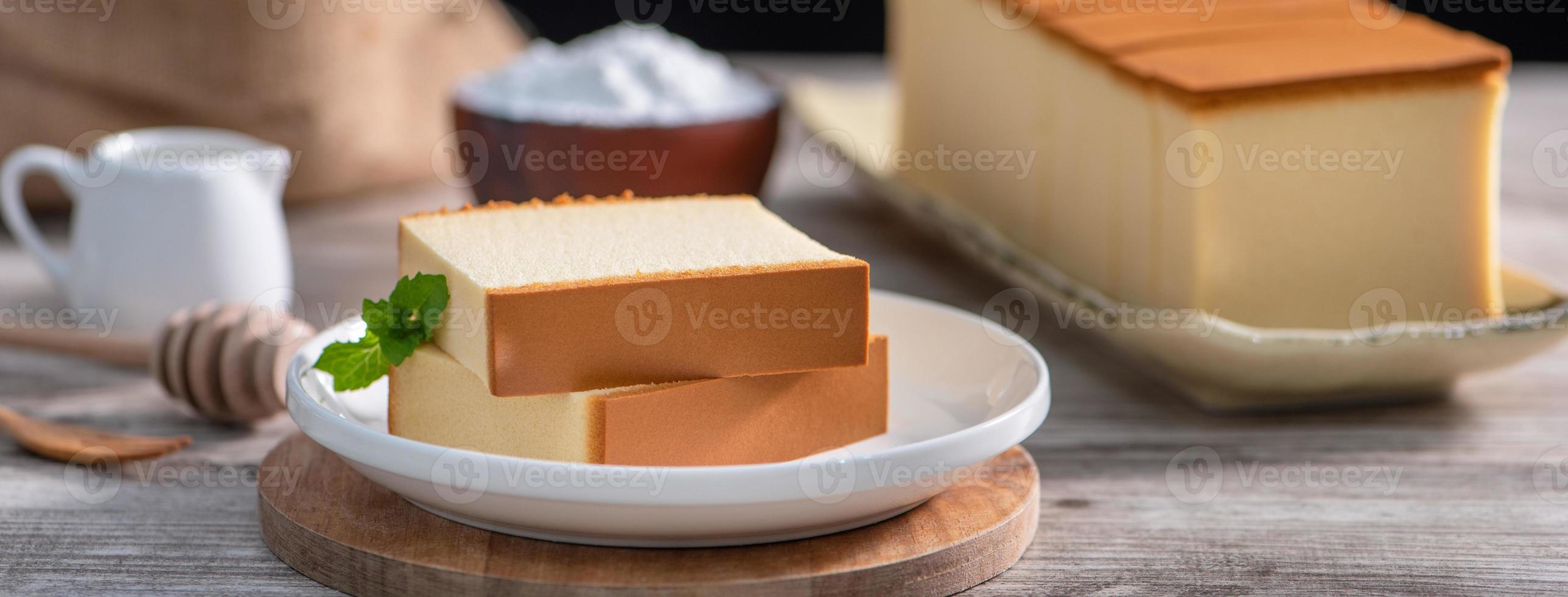 Castella - köstliches japanisches, in Scheiben geschnittenes Biskuitkuchenessen auf weißem Teller über rustikalem Holztisch, Nahaufnahme, gesunde Ernährung, Kopierraumdesign. foto