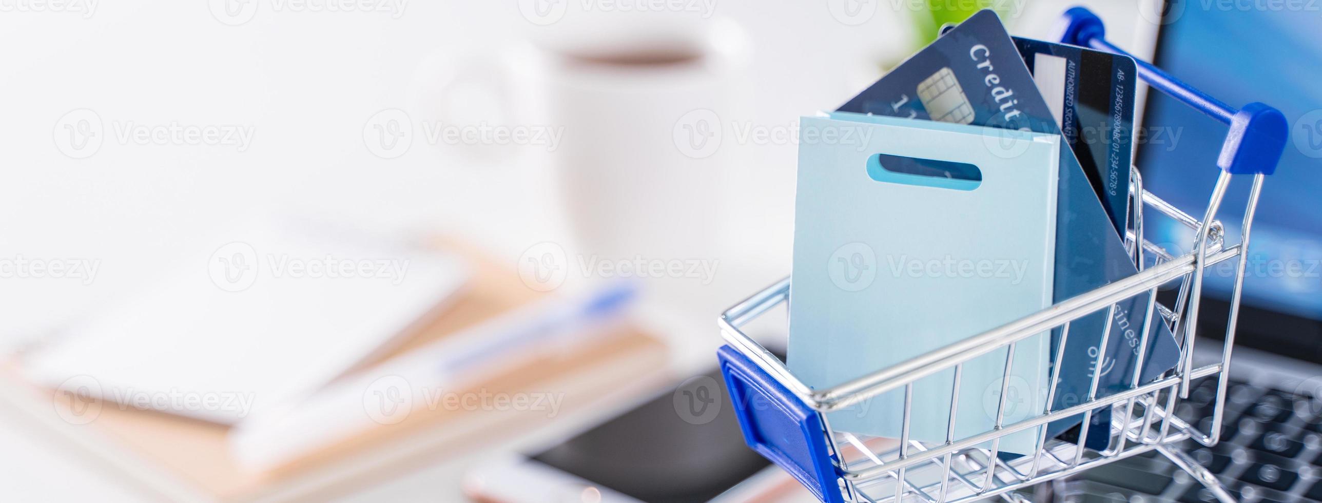 Online-Zahlung im Büro, Einkaufen zu Hause bleiben, elektronische Zahlung mit Kreditkartenkonzept, Laptop auf weißem Tischhintergrund mit Einkaufswagen, Nahaufnahme. foto