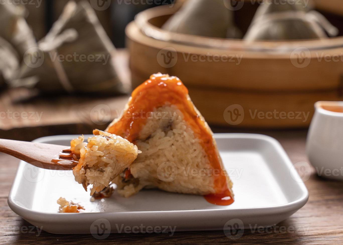 Dragon Boat Festival Essen - Reisknödel Zongzi, junge asiatische Frau, die chinesisches traditionelles Essen auf Holztisch zu Hause isst, Feier, Nahaufnahme foto