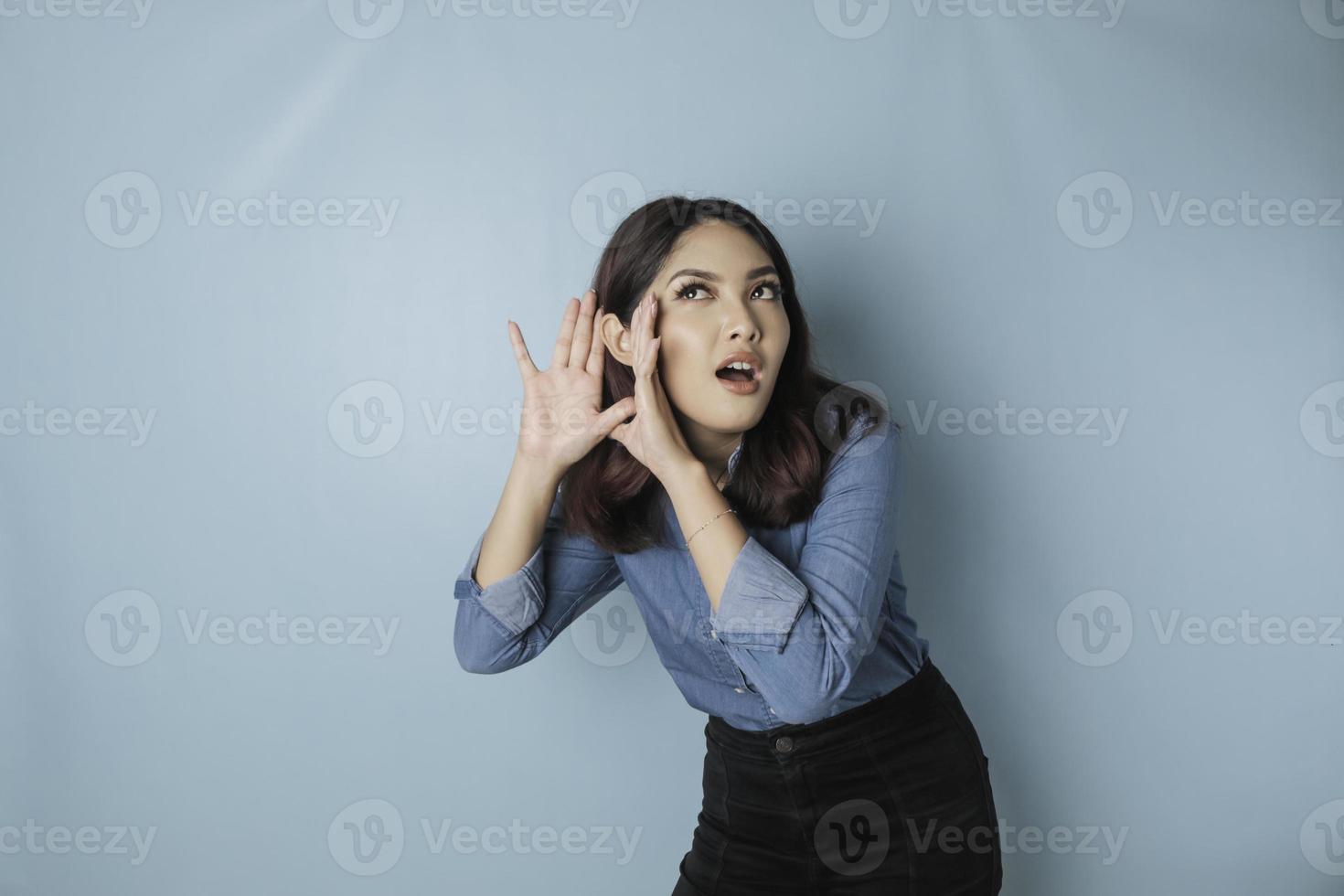 erstaunte neugierige Braut junge Frau, die ein blaues Hemd trägt und versucht, Sie zu hören, wie Sie aufmerksam zuhören, isoliert auf blauem türkisfarbenem Hintergrund Studioportrait. foto