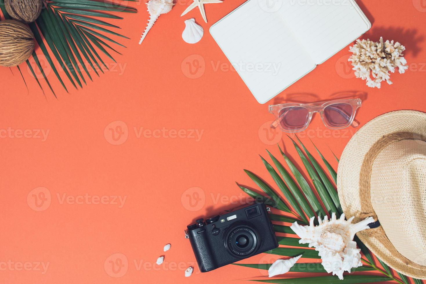 Bunte Sommerferienmode flach lag - Strohhut, Kamera, Sonnenbrille, Muscheln auf leuchtend orangefarbenem Hintergrund foto