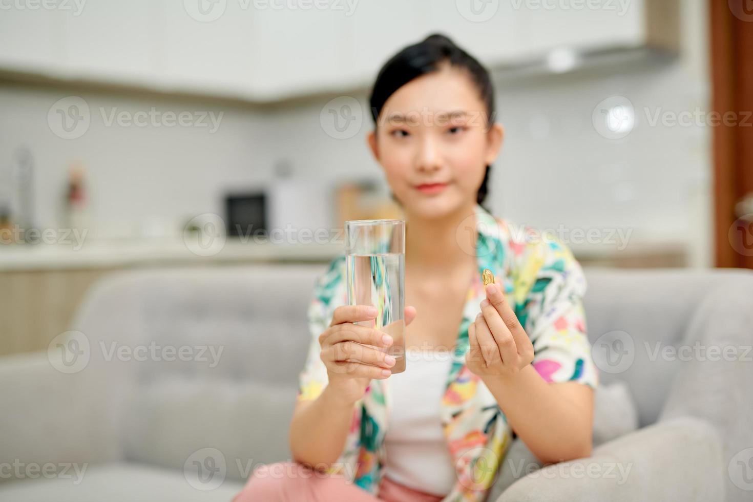 glückliche frau, die eine vitamingelbe pille einnimmt, die zu hause auf einer couch im wohnzimmer sitzt foto