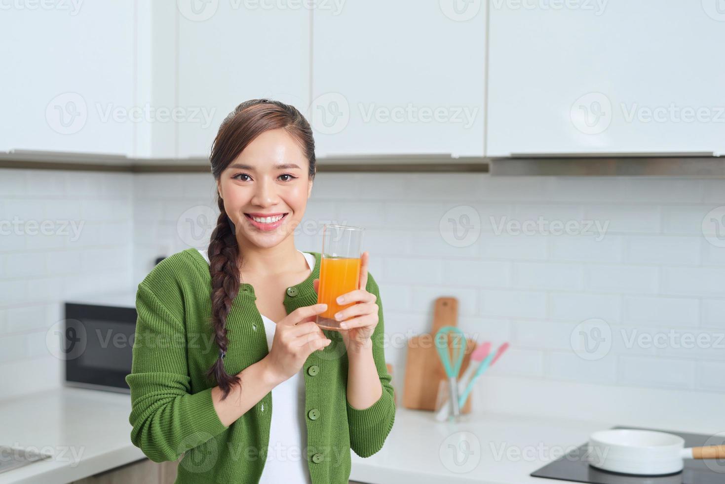 attraktive Frau, die ein Glas Orangensaft hält, während sie in der Küche steht foto