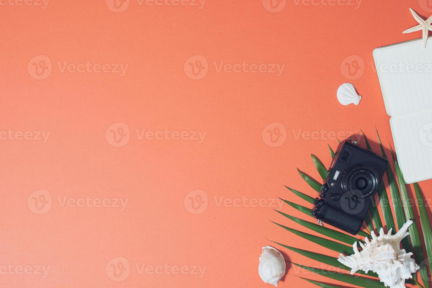 Bunte Sommerferienmode flach lag - Strohhut, Kamera, Sonnenbrille, Muscheln auf leuchtend orangefarbenem Hintergrund foto