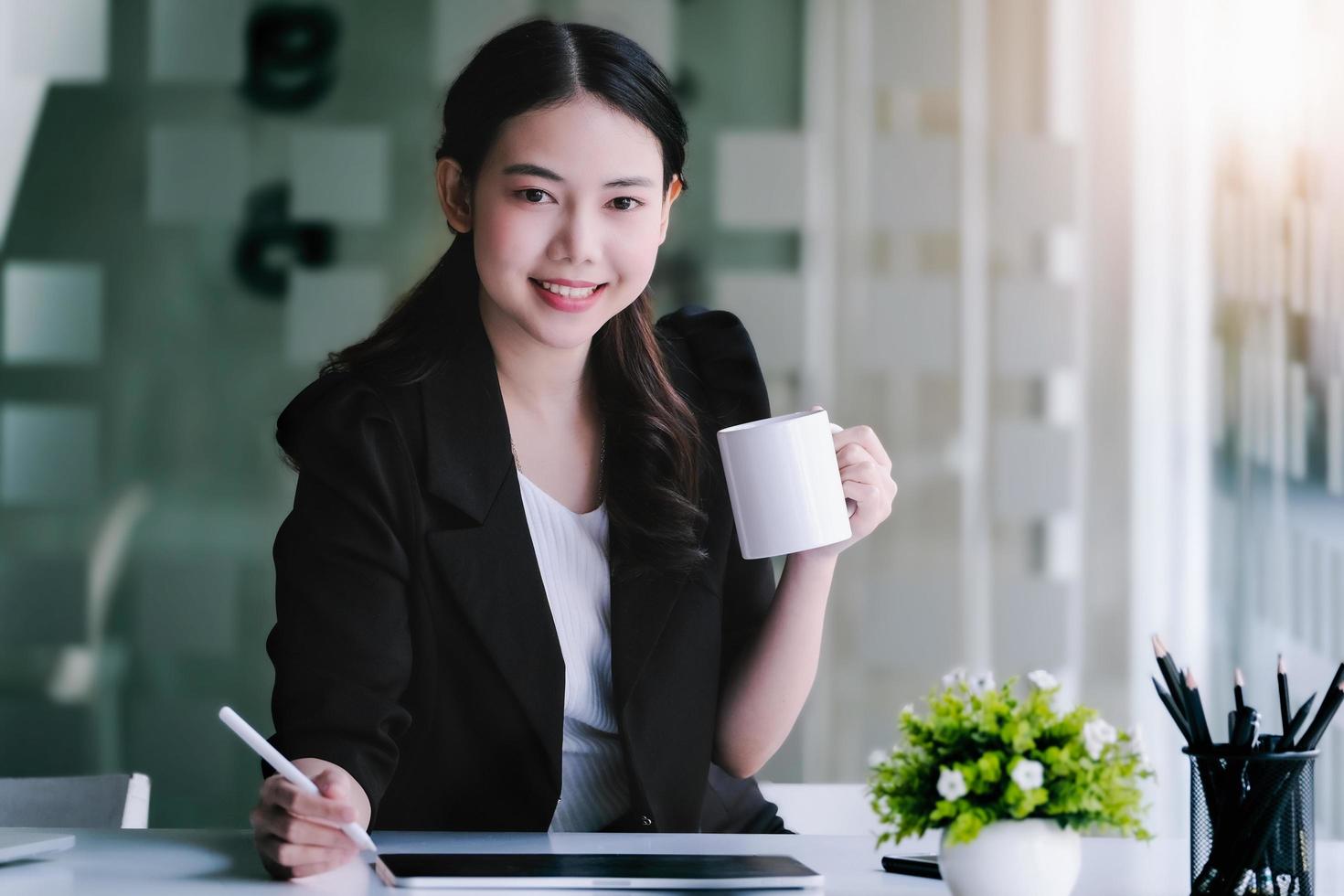 Weibliche Marketingmanager trinken Kaffee, während sie arbeiten, um Schläfrigkeit zu reduzieren, bevor sie Tablet-Computer und Marketinganalysepapiere verwenden. foto