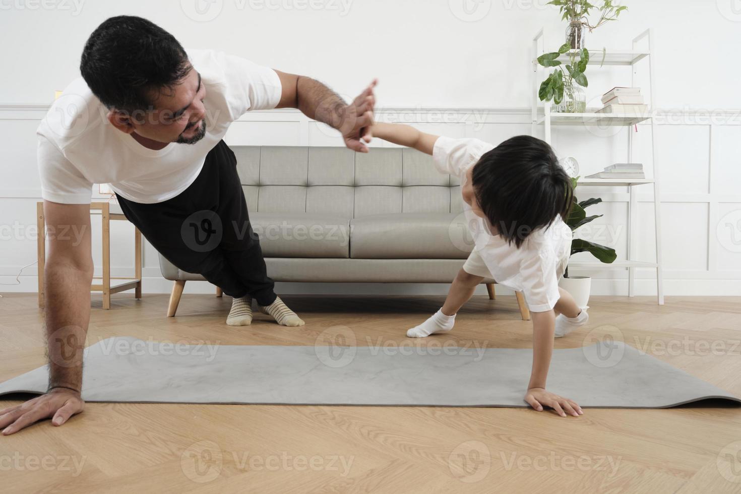 junge asiatische thailändische vater lieblich trainiert ihren kleinen sohn zu trainieren und praktiziert yoga auf dem boden des wohnzimmers zusammen für gesunde fitness und wellness, glücklicher häuslicher lebensstil an familienwochenenden. foto