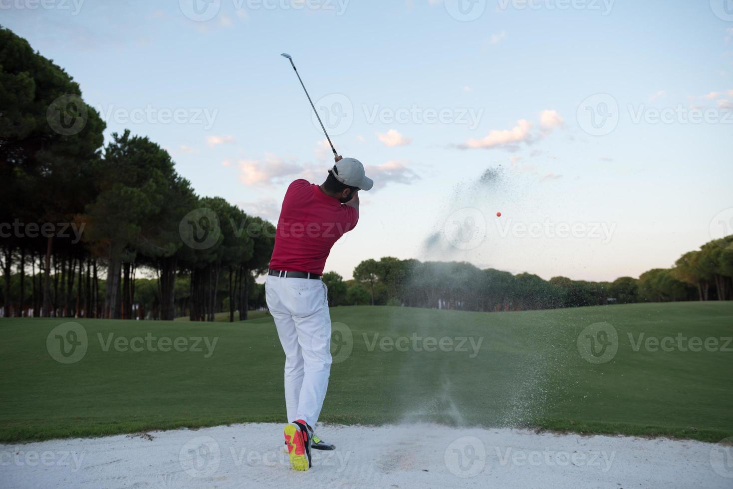 Golfspieler, der einen Sandbunker schlägt, der bei Sonnenuntergang erschossen wird foto