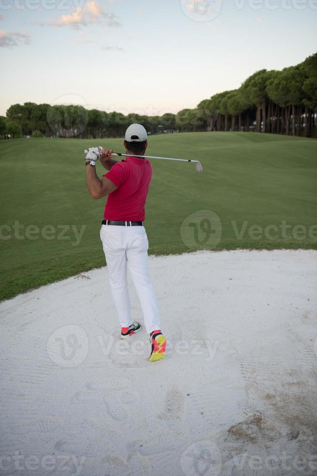 Golfspieler, der einen Sandbunker schlägt, der bei Sonnenuntergang erschossen wird foto