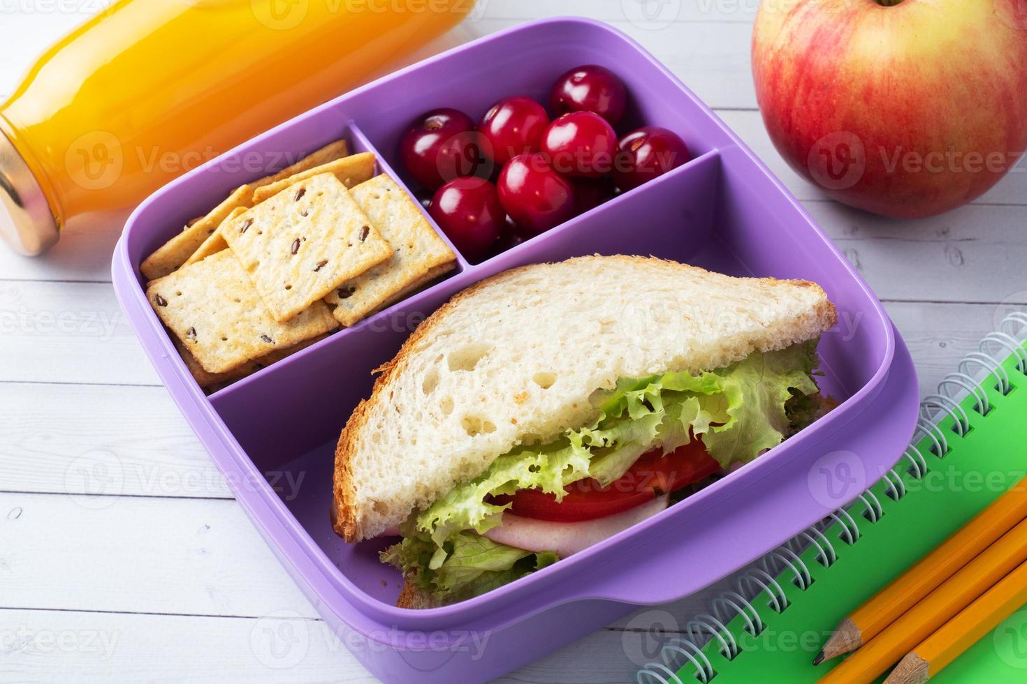 leckeres gesundes Sandwich in einer Brotdose, Keksen und Kirschen. Mittagessen mit in die Schule oder ins Büro nehmen. Saft in einer Flasche und einem Apfel. foto