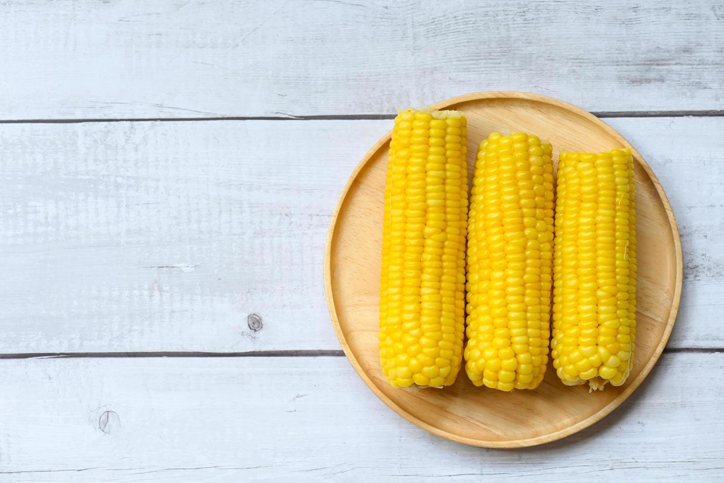 Gekochter Zuckermais auf Holzplattenhintergrund, reife Maiskolben gedämpft oder gekochter Zuckermais für veganes Abendessen oder Snack foto