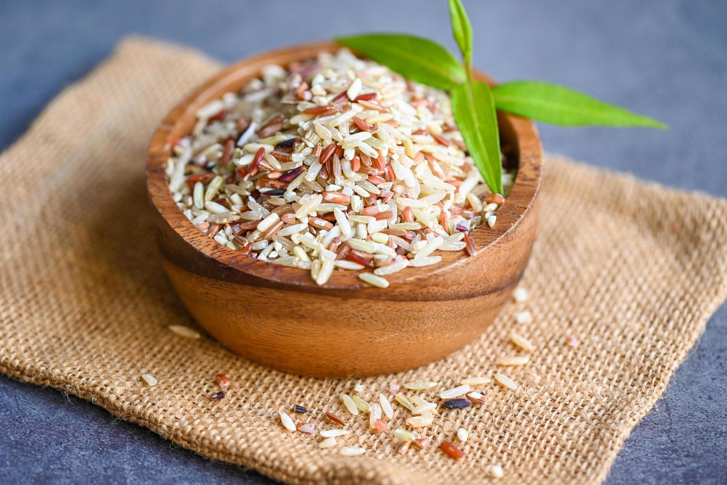 rohe verschiedene Reisfarbe gemischter thailändischer Reis zum Kochen von Speisen, Loonzain-Reis braun schwarz rot weiß lila Biokost, brauner Reis auf Holzschale und grünes Blatt foto