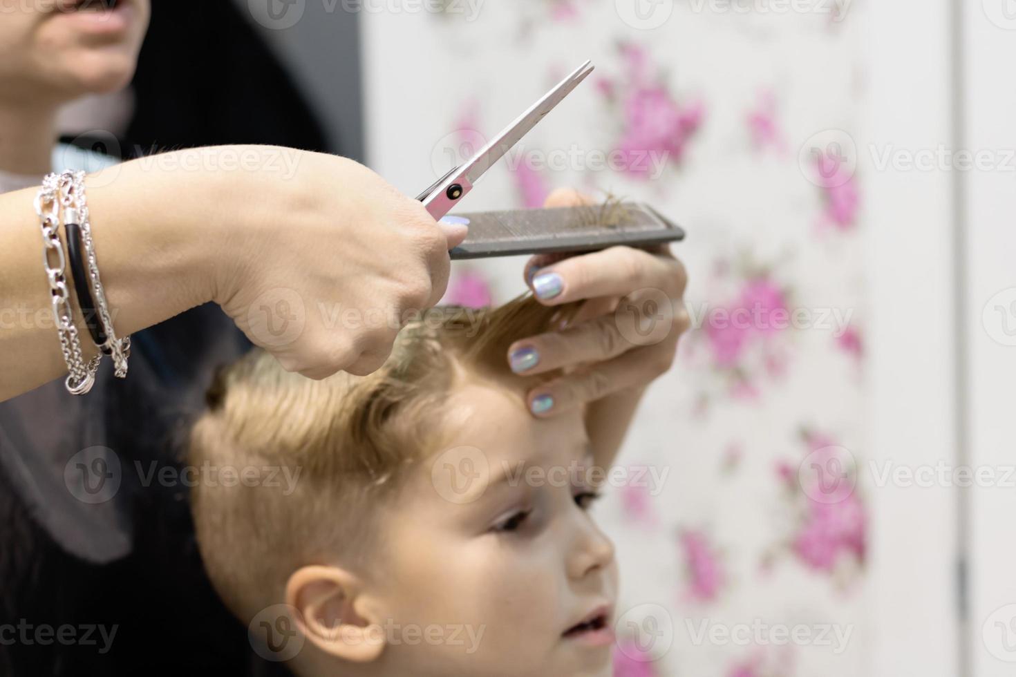 Nahaufnahme des Friseurs, der im Salon die Haare des Jungen schneidet. foto