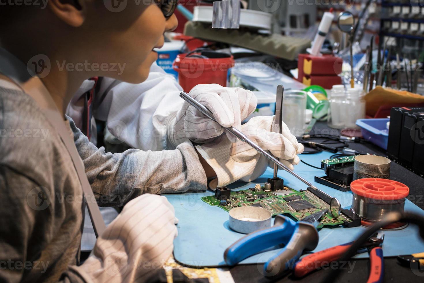 Kleiner Junge, der mit Hilfe eines Lehrmeisters im Tech-Labor Leiterplatten repariert. foto