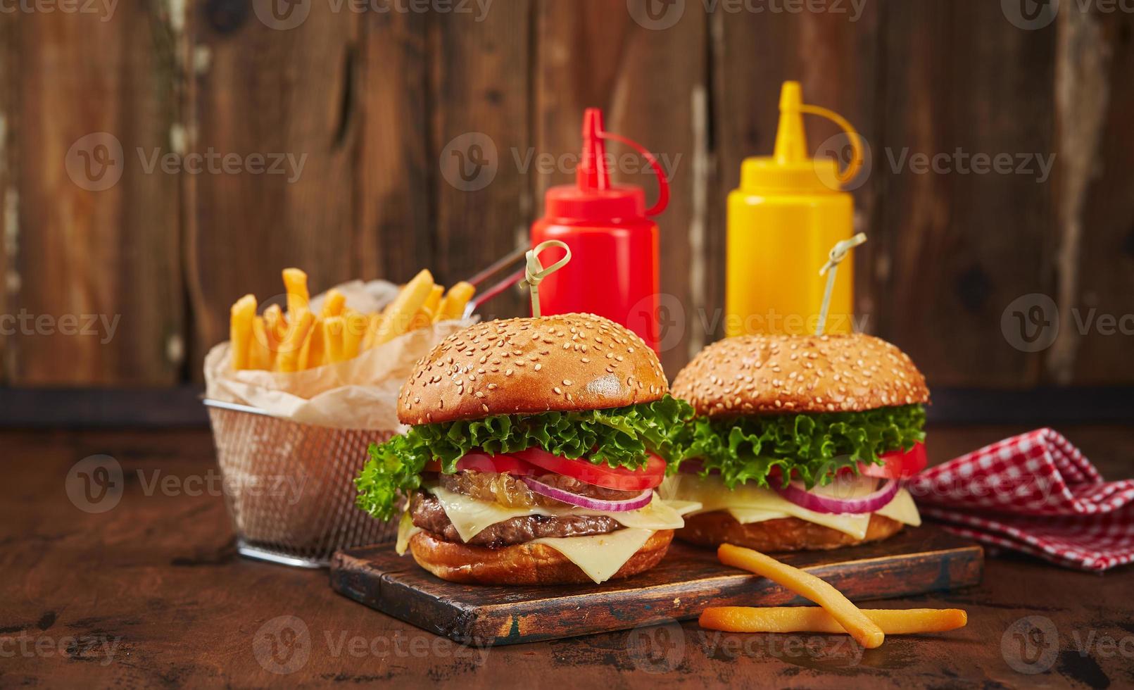 zwei hausgemachte Burger mit Rindfleisch, Käse und Zwiebelmarmelade auf einem Holzbrett, Pommes im Metallkorb und Saucen. fast-food-konzept, amerikanisches essen foto