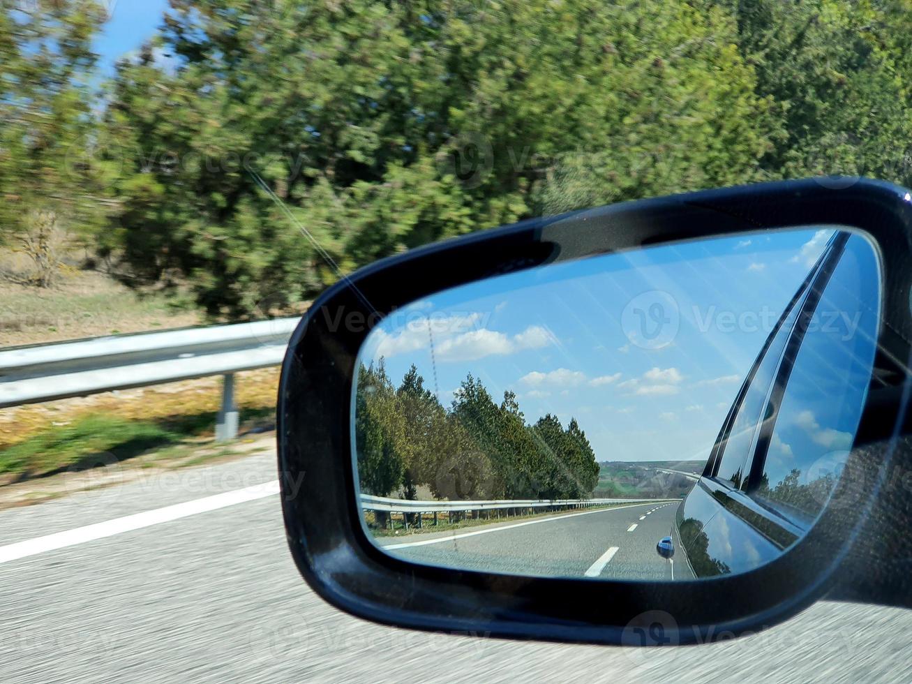 Landschafts- und Straßenreflexion im schwarzen Rückspiegel des Autos. foto