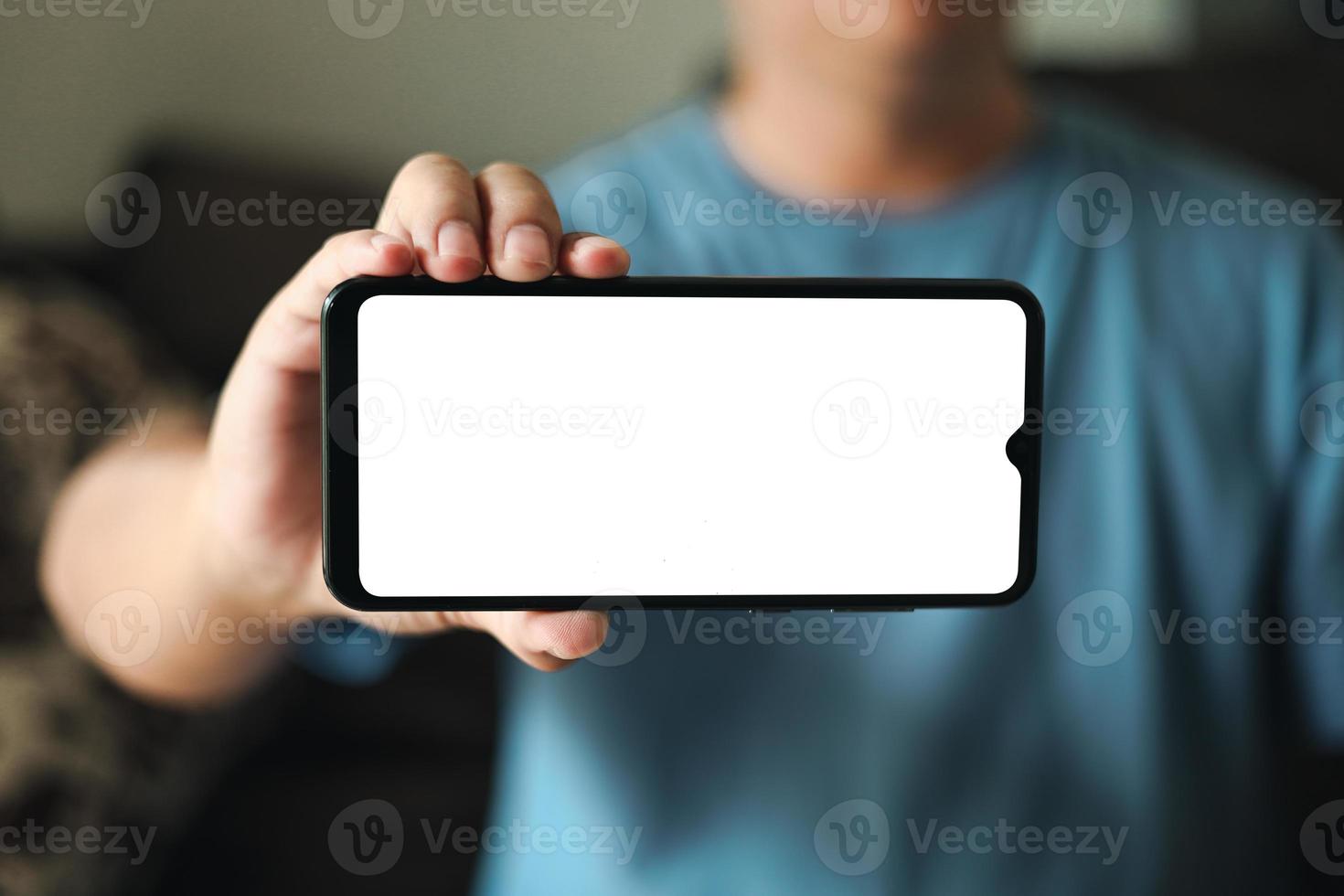 Smartphone-Präsentation mit leerem Bildschirm. ein junger mann hält ein telefon mit einem weißen leeren bildschirmmodell. ein mann trägt ein blaues t-shirt im wohnzimmer zu hause. foto
