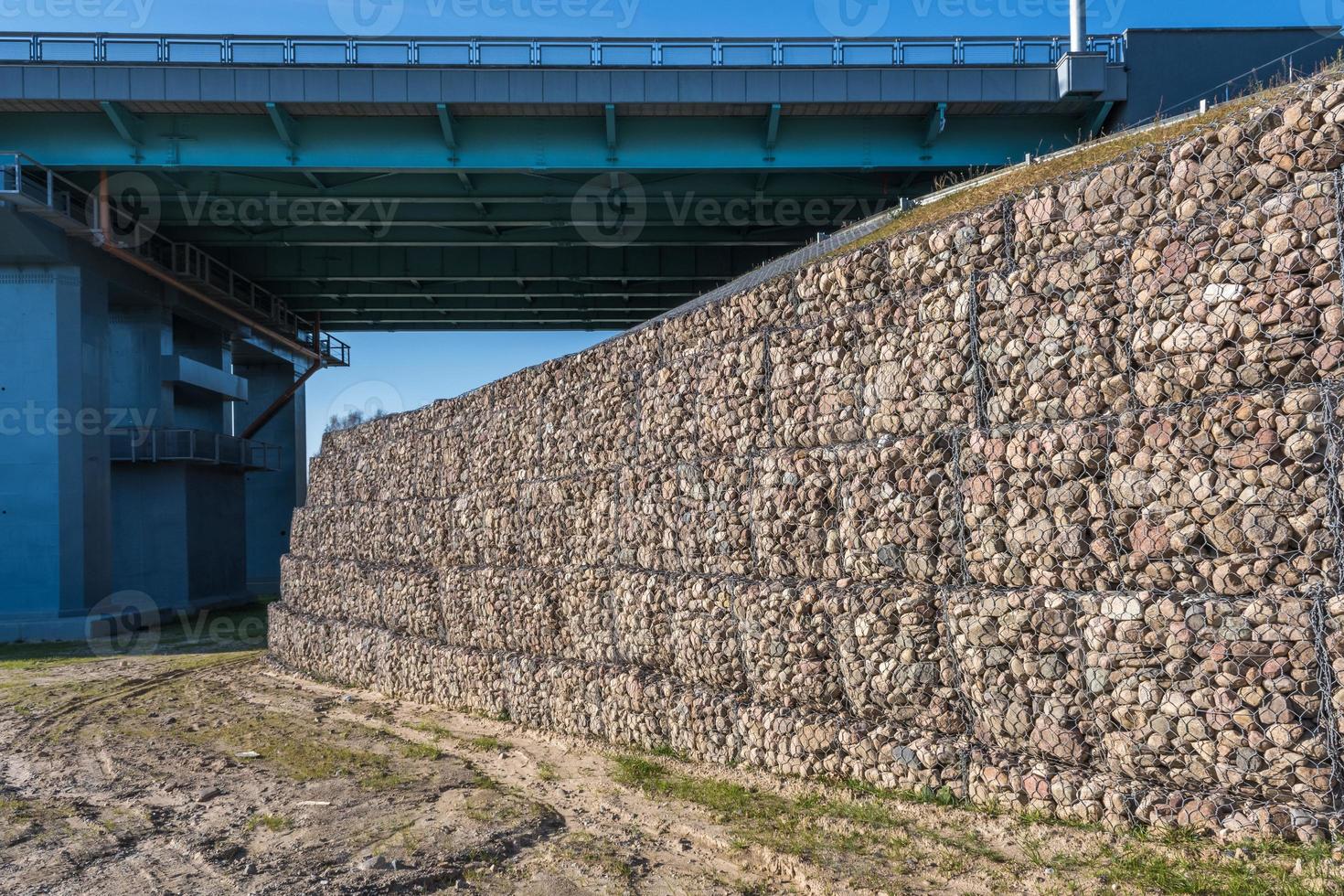 Ingenieurbauwerk aus Steinen hinter Metalldrahtnetzen zur Befestigung des Flussufers in der Nähe der Straßenbrücke foto