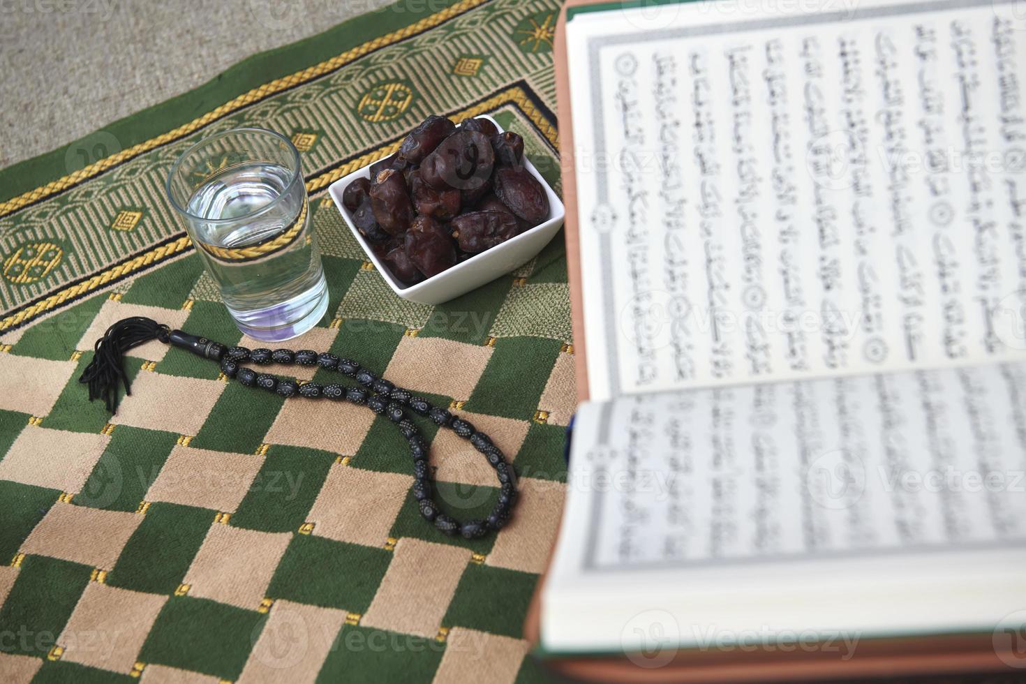 iftar-zeit getrocknete datteln heiliger koran glas wasser und tasbih auf betendem teppich oder sejadah foto