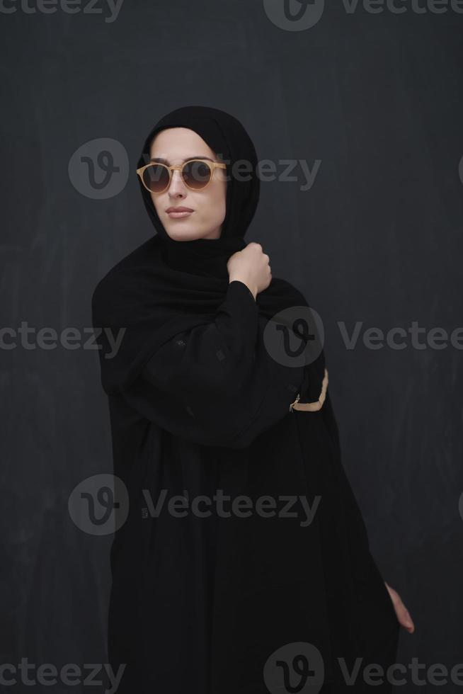 junger muslim in traditioneller kleidung oder abaya und sonnenbrille posiert vor schwarzer tafel foto