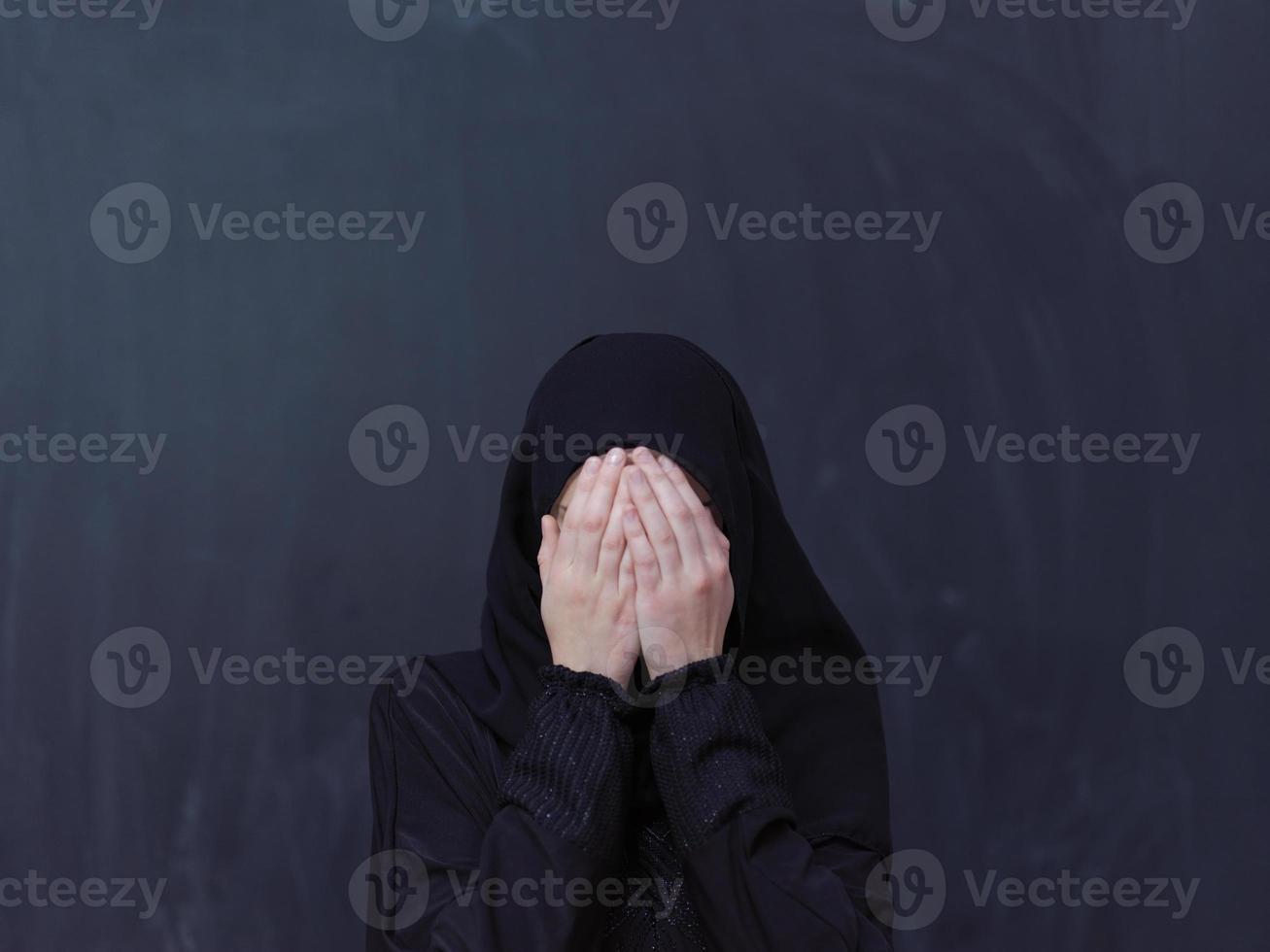 muslimische frau, die traditionelles beten zu gott vor schwarzer tafel macht foto