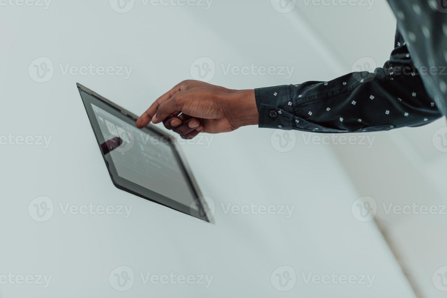 Lächelnder afroamerikanischer Mann mit modernem Smart-Home-System, Controller an der Wand, positiver junger Mann, der die Temperatur am Thermostat schaltet oder Sicherheitsalarm in der Wohnung aktiviert foto